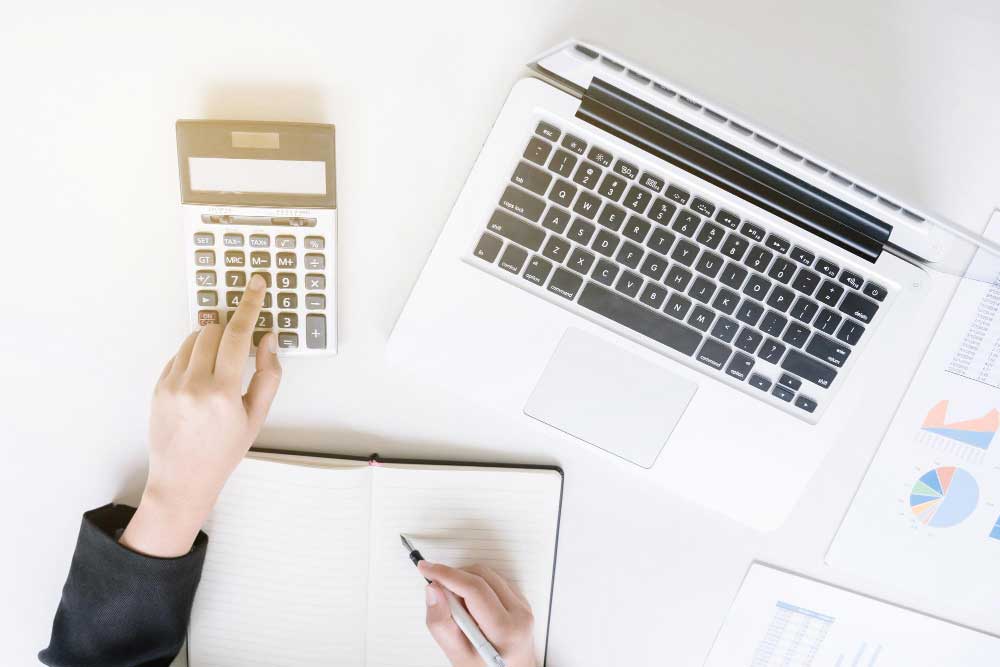 bookkeeping services miami professional calculating finances with a calculator, laptop, and financial reports on a clean office desk