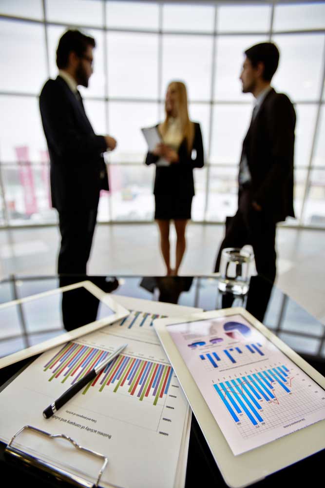 business-financial-consultant-6 Financial reports on a conference table with professionals meeting in the background, showcasing expert business financial consultant Fort Lauderdale services