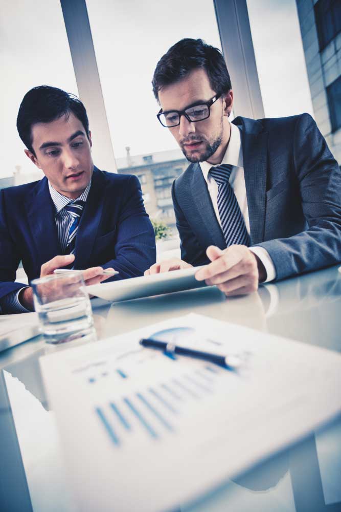 business-consulting-firms-miami Two executives reviewing financial documents and reports with guidance from a business financial consultant miami in a corporate office